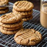 Several homemade chewy peanut butter cookies stacked on a cooling rack with a jar of peanut butter in the background.