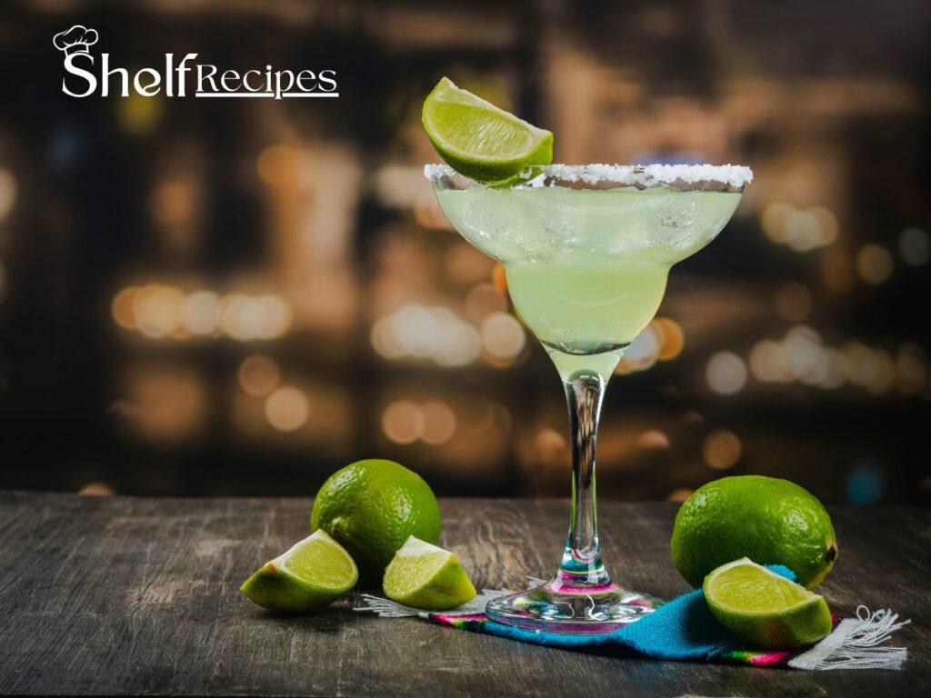 A refreshing margarita garnished with a lime wedge and surrounded by fresh lime slices on a wooden table, with a blurred city lights background.
