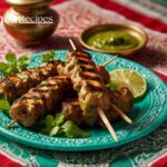 Golden Bahraini Kebabs on a plate with mint chutney, garnished with cilantro, on a vibrant Bahraini tablecloth