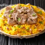 Jordanian mansaf dish with lamb on yellow rice, garnished with almonds and parsley, served on a decorative metal platter.