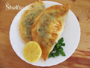 Two Tunisian brik pastries filled with egg and herbs on a white plate, garnished with a lemon wedge and parsley, on a wooden table.