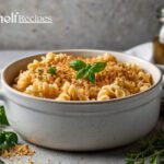 A serving of creamy blue cheese pasta bake topped with golden breadcrumbs, garnished with fresh herbs, in a white ceramic dish