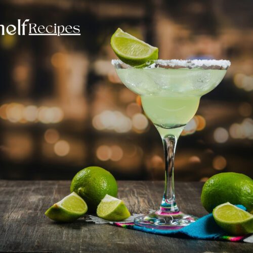 A refreshing margarita garnished with a lime wedge and surrounded by fresh lime slices on a wooden table, with a blurred city lights background.